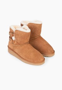 Stivaletti alla caviglia in suede marrone foderati in morbida lana crema. Punta rotonda, suola in gomma spessa e bottoni decorativi sul lato.