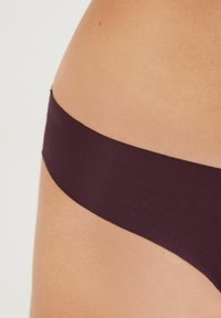 Ciemnofioletowe majtki z rozciągliwego materiału z gładką, szeroką gumką w pasie. Materiał wydaje się miękki, z bezszwowym wzornictwem, ukazanym w okolicy bioder.