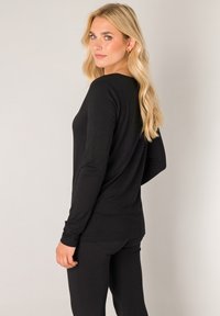 Black long-sleeve top with a relaxed fit, smoothly textured fabric, and rounded neckline, paired with matching black pants.