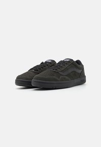 Black suede sneakers with a textured finish, featuring a thick black rubber sole and subtle zigzag stitching along the edges.