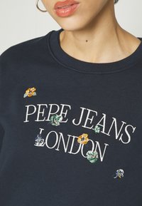 Sweat-shirt bleu marine avec le texte brodé "PEPE JEANS LONDON", agrémenté d'accents floraux colorés en jaune, vert et bleu. Texture lisse.
