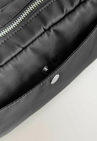 Borsetta di tessuto nero con una texture liscia, dotata di una cerniera argentata e di una chiusura a scatto in metallo. L'interno è sfoderato e spazioso.
