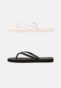Witte en zwarte rubberen slippers met een gestructureerde voetbed, dunne bandjes en contrasterende kleuren. Elk paar heeft een eenvoudig ontwerp en minimale branding.