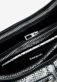 Black and white snake-print handbag with multiple zippered pockets, textured exterior, and a visible label reading "Desigual."