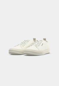 Bílé plátěné tenisky s texturovanou gumovou podrážkou, šněrovacím designem a zadním poutkem. Minimalistický styl bez viditelných vzorů nebo akcentů.