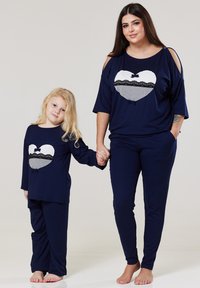 Zladená súprava loungewear v námořní farbe pre dospelých a deti, s grafickým motívom srdca a čipkovým lemovaním. Mäkka tkanina, voľný strih, dlhé rukávy a nohavice.