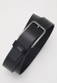 Svart lærbelte med en glatt tekstur, med en sølv rektangulær spenne og merkevaredetalj. Minimalistisk design med hull.