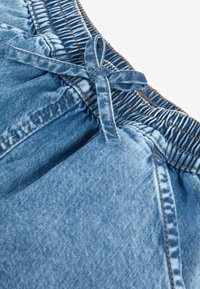 Jeansshorts med en blå tvätt, med en elastisk midja och snörning samt synliga sömdekorationer längs sömmarna.