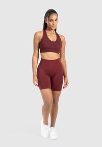 Bordeaux sportbeha en set van hoge taille shorts in een gladde, rekbare stof. Beha heeft brede bandjes; shorts zijn aangesloten en knielang.