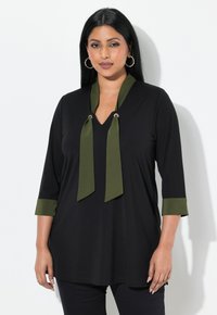 Zwarte tuniek met een V-hals en olijfgroene strikjes bij de kraag. Driekwart mouwen met olijfgroene manchetten. Zacht, glad materiaal.