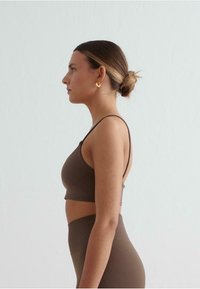 Bruine crop top en hooggeladen leggings gemaakt van gladde, rekbare stof. Dunne bandjes en naadloos ontwerp, tegen een eenvoudige achtergrond.