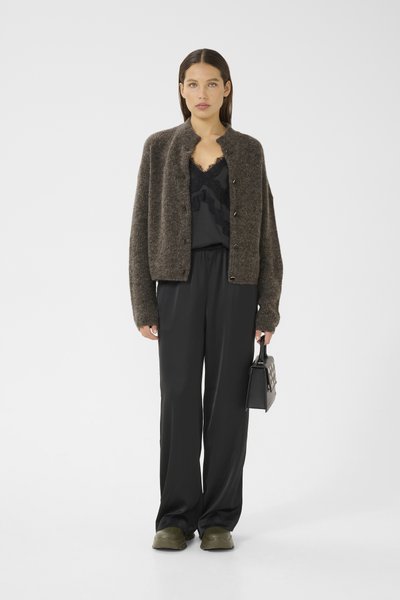 Cardigan en tricot marron avec un col rond et des boutons, superposé à un haut noir avec des bordures en dentelle. Pantalons noirs à jambe large et un petit sac à main noir.