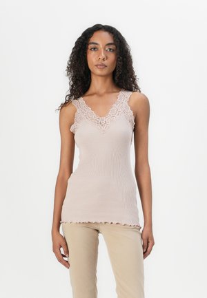 Lichtroze geribbelde tanktop met kantdetails langs de halslijn, gegolfde zoom en dunne bandjes. Gekozen in combinatie met beige broeken.