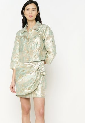 Set di giacca corta e gonna mini in tessuto iridescente menta con dettagli dorati, caratterizzato da un collo a camicia e un dettaglio attorcigliato sulla gonna.