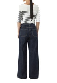 Wijdvallende denim broeken in donkerblauw met een hoge taille en contrasterende gouden stiksels; wit en marineblauw gestreept shirt met driekwart mouwen.