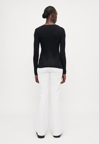 Schwarzes, geripptes Langarmshirt mit weitem Ausschnitt, kombiniert mit weißen, ausgestellten Hosen, die eine glatte Textur und eine figurbetonte Silhouette zeigen.