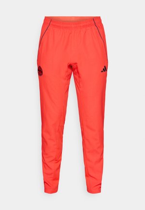 Rode sportbroek met taps toelopende pasvorm, elastische tailleband, zijzakken en contrasterende marineblauwe accenten. Voorzien van een logo op de linker dij.