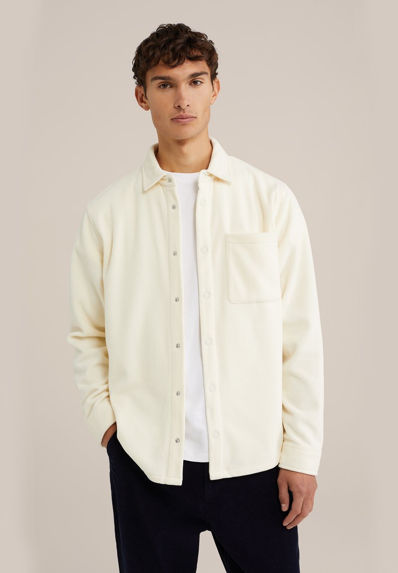Cream-colored fleece shirt jacket with a relaxed fit, front pocket, and snap-button closure, worn over a white crewneck T-shirt.