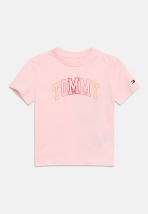 Rosa T-Shirt für Kleinkinder mit kurzen Ärmeln, auf dem "TOMMY" in mehrfarbigen Blockbuchstaben und ein kleines Flaggenlogo auf dem linken Ärmel zu sehen ist.