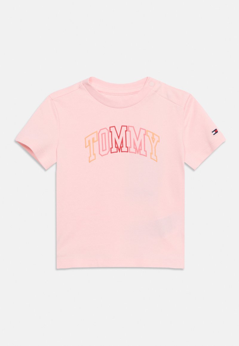 T-shirt pour tout-petit à manches courtes rose avec "TOMMY" écrit en lettres blocs multicolores et un petit logo drapeau sur la manche gauche.