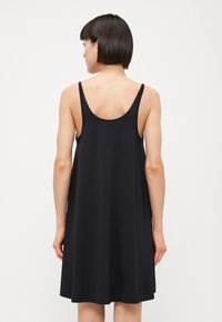 Vestido negro sin mangas hecho de una tela ligera, con un corte relajado y una espalda con escote, diseñado para caer por encima de las rodillas.