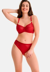 Ensemble de lingerie rouge comprenant un soutien-gorge avec armatures et des bretelles réglables, associé à une culotte taille haute assortie. Tissu lisse et extensible.