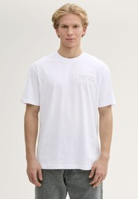 Witte katoenen t-shirt met korte mouwen, voorzien van een klein bedrukt logo in grijze tekst op de linkerborst. Eenvoudig, klassiek ontwerp.