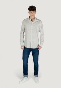 Camicia bianca a maniche lunghe con un colletto button-down, abbinata a jeans blu e sneakers bianche, che mostra un look casual.