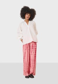 White, long-sleeve pullover with a V-neck; paired with pink tie-dye wide-leg pants featuring vertical stripes; black sandals.