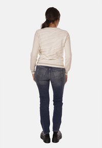 Maglione beige con texture cremosa e un motivo ondulato, abbinato a jeans slim-fit blu scuro e scarpe nere, visto da dietro.