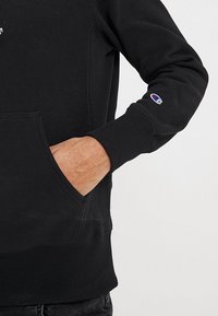 Sudadera negra con un acabado texturizado, un bolsillo frontal, puños de canalé y un pequeño logo en la manga.