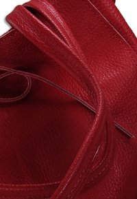 Rode leren handtas met een gestructureerde afwerking. Heeft gebogen handvaten en zichtbare stiksels langs de randen. Het interieur is ruim en glad.