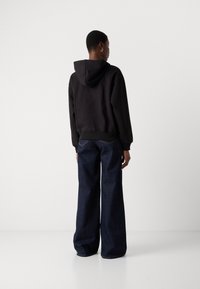 Black cotton hoodie with a hood and ribbed hem, paired with wide-leg dark denim jeans featuring back pockets and contrasting stitching.
