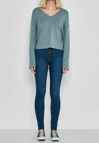Maglione blu chiaro a collo a V, corto e con maniche lunghe, abbinato a jeans skinny blu scuro con vita alta e chiusura a cinque bottoni.