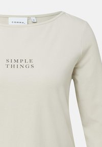 Beżowa bluzka z długim rękawem, z okrągłym dekoltem oraz nadrukowanym napisem "SIMPLE THINGS" w ciemnej czcionce. Wykonana z miękkiej, gładkiej bawełny.
