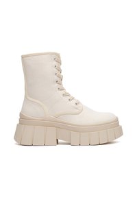Bota tobillera de lona beige con una suela gruesa y plana. Cuenta con cordones delanteros, costuras reforzadas y textura suave. Diseño con punta redondeada.