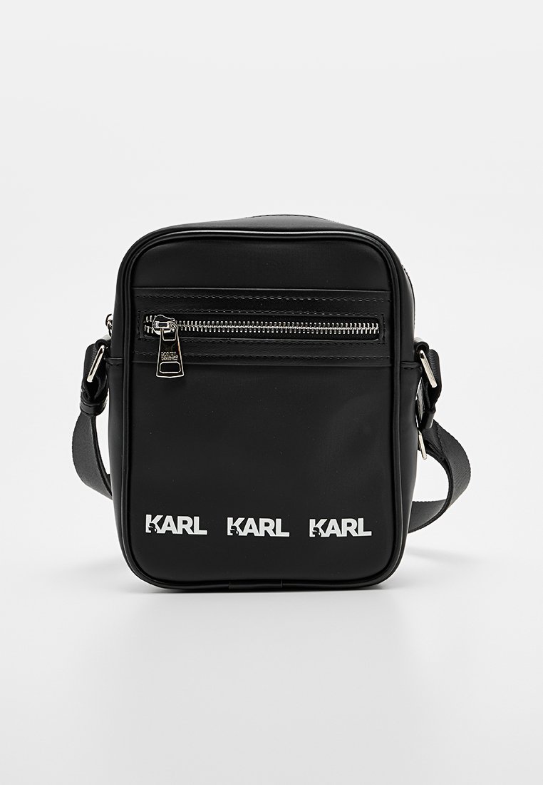 Bolso mensajero negro hecho de material suave, con un bolsillo frontal con cremallera, correa ajustable y la marca "KARL" repetida en blanco.