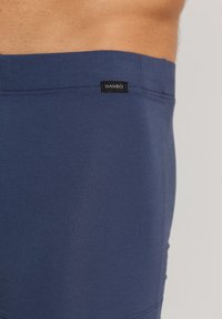 Boxer breifs de algodón azul con una textura suave, cinturilla elástica y una pequeña etiqueta negra con "HANRO" cerca de la parte superior.