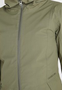 Veste vert olive en tissu doux et imperméable, dotée d'une fermeture éclair frontale, d'une capuche et d'un logo discret sur le côté.