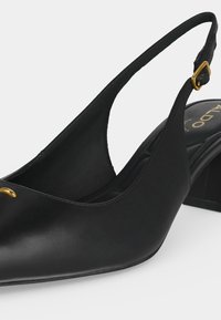 Escarpin slingback en cuir noir avec bout pointu, petit talon bloc et boucle dorée sur bride réglable.
