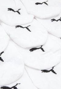 Calcetines tobilleros blancos de algodón con un patrón del logo negro de Puma. Varios pares apilados, mostrando una textura suave y un ajuste ceñido.