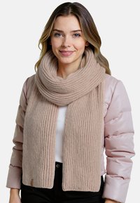 Strikket tørklæde i lys beige, har ribbet tekstur, bredere ender og et foldet design. Båret sammen med en lys rosa pufferjakke.