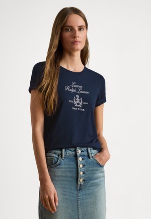 T-shirt en coton bleu marine avec manches courtes retroussées et logo blanc imprimé ; associé à une jupe en denim bleu clair avec détail de boutons.