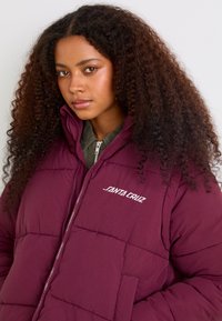 Purple puffer jacket with quilted design, featuring a front zipper, high collar, and white "Santa Cruz" logo on the left chest.
