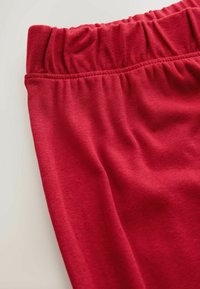 Pantaloni roșii din bumbac, prevăzuți cu talie elastică cu textură adunată, material neted și o croială lejeră. Vedere de aproape care evidențiază detaliile designului.