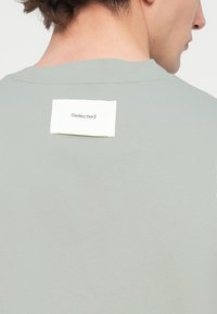 Ανοιχτό πράσινο t-shirt με στρογγυλή λαιμόκοψη και κοντά μανίκια· διαθέτει ορθογώνια ετικέτα με κείμενο "Selected" στην πλάτη. Απαλή υφή.