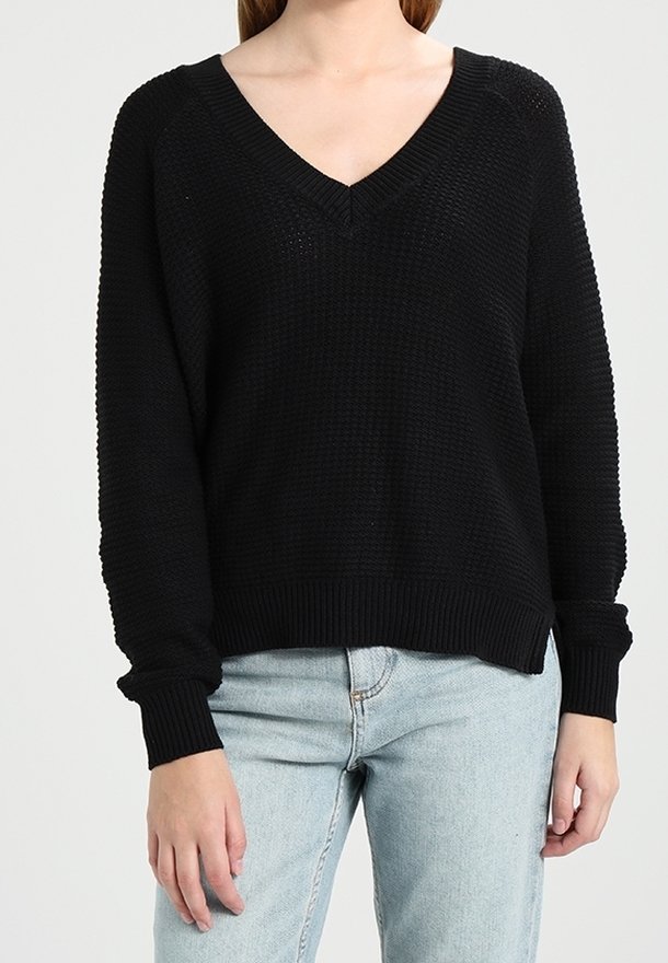 Musta neulepaita V-kaula-aukkolla, teksturoidusta kankaasta, resorireunuksilla hihoissa ja helmassa, rento istuvuus, yhdistetty vaaleansinisten farkkujen kanssa.