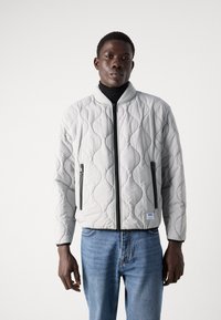 Light grey quilted bomber jacket with a high collar, zippered front, and side pockets; features a textured pattern and contrasting black zippers.