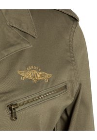 Veste olive en finitions texturées, dotée d'une poche zippée sur la poitrine et d'un emblème d'aile brodé en or avec "SCHOTT" et "1913".