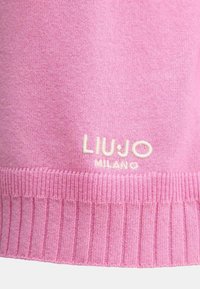 Maglione rosa lavorato a maglia con orlo a coste, che presenta un sottile logo crema "LIU JO MILANO" vicino al fondo. Texture morbida, materiale leggero.